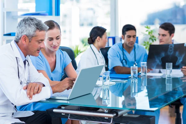 Läkare och sjuksköterska tittar på laptop med kollegor bakom — Stockfoto