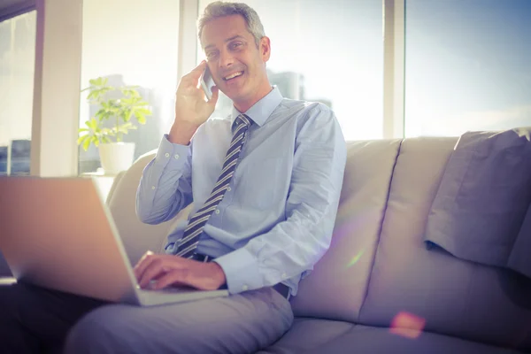 Businessman sitting on a couch having phone call — Stock Photo, Image
