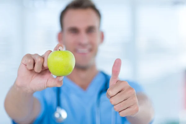 Medico sorridente che presenta una mela verde — Foto Stock