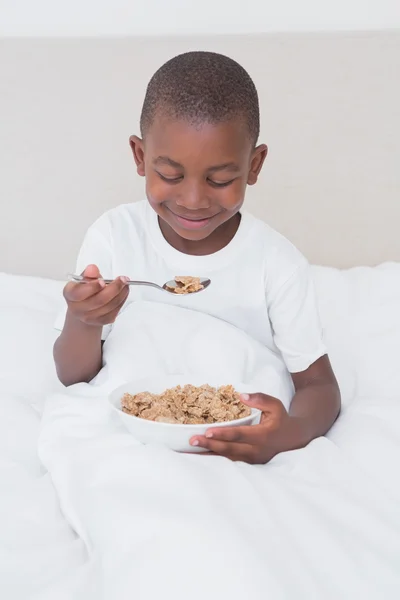 Krásný malý chlapec jíst obiloviny v posteli — Stock fotografie