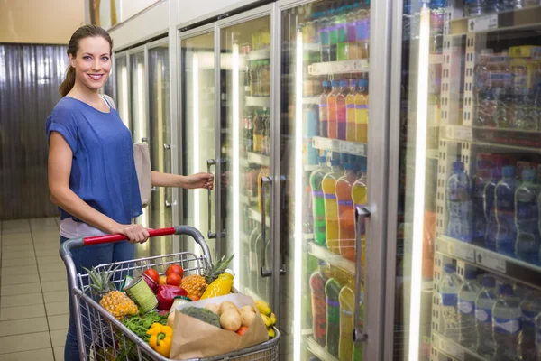 Mooie vrouw kijken naar de camera en nemen product op koelkast — Stockfoto