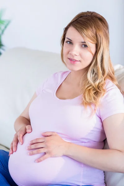Schwangere blickt mit den Händen am Bauch in die Kamera — Stockfoto