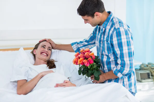 Hombre ofreciendo flores a la mujer embarazada en el hospital —  Fotos de Stock