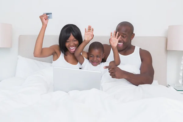 Feliz sonrisa bonita pareja usando el ordenador portátil con su hijo en la cama —  Fotos de Stock