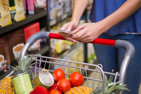 Bella donna spingendo carrello in corridoio e sms — Foto Stock