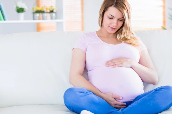 Беременная женщина сидит на диване и трогает живот. — стоковое фото