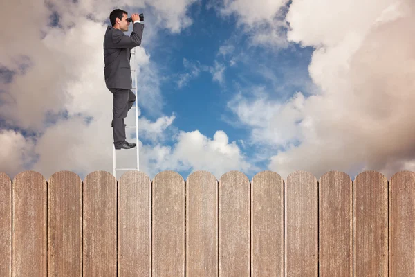 Businessman standing on ladder and using binoculars — Stock Photo, Image