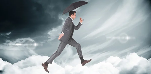 Businessman jumping and holding umbrella — Stock Photo, Image