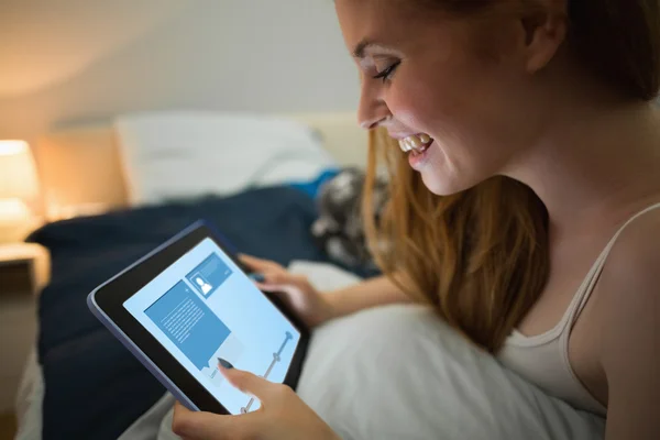 Rotschopf mit Tablette auf ihrem Bett liegend — Stockfoto