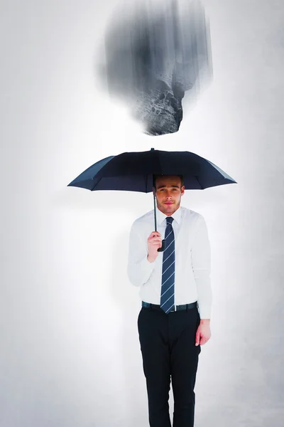 Businessman sheltering under umbrella Stock Image