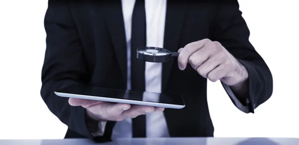 Businessman looking at his tablet through magnifying glass — Stock Photo, Image