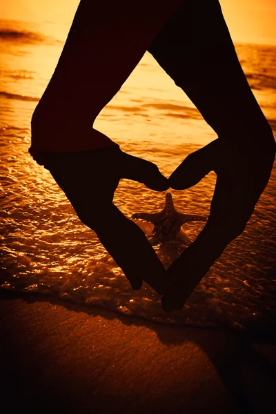 Руки, формирующие сердце против морской звезды — стоковое фото