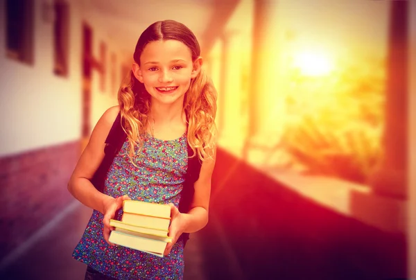 Imagen compuesta de una linda niña sosteniendo libros en la biblioteca —  Fotos de Stock