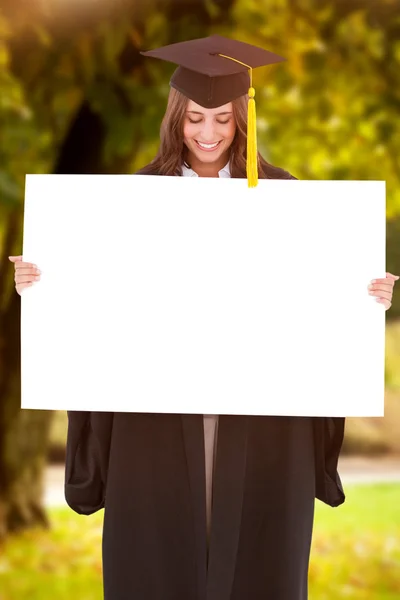 Imagen compuesta de una mujer sonriente mientras sostiene y mira una b — Foto de Stock