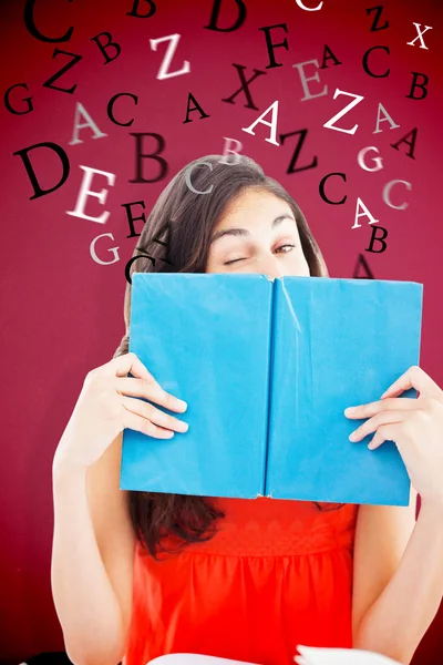 Student winking behind a blue book — Stock Photo, Image