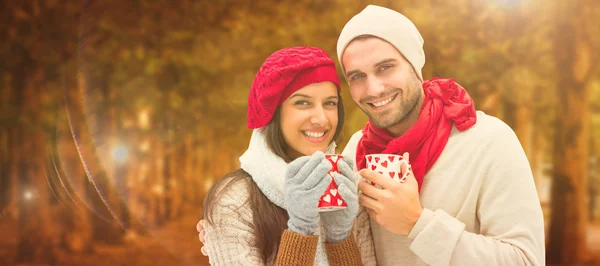 Composite image of winter couple holding mugs — Stock Photo, Image