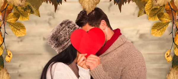 Jovem casal beijando atrás de coração vermelho — Fotografia de Stock