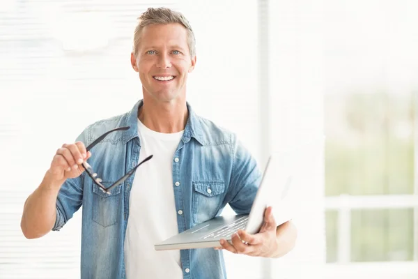 Hombre de negocios sonriente sosteniendo una computadora portátil — Foto de Stock