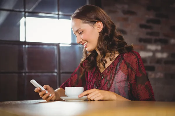 Bruna sorridente che beve caffè e messaggia — Foto Stock