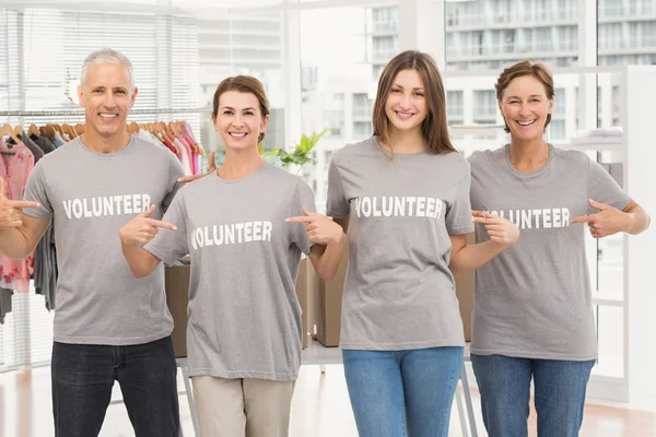 Улыбающиеся добровольцы, указывающие на свои рубашки — стоковое фото