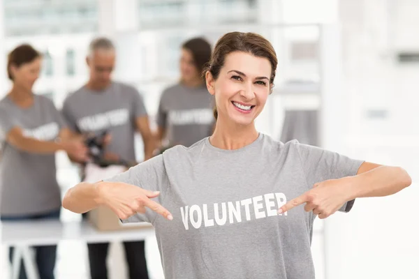 Smiling voluntária feminina apontando na camisa — Fotografia de Stock