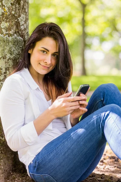 Brunette verzenden van tekst in het park — Stockfoto