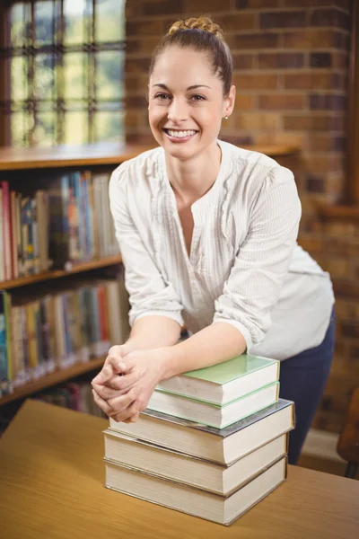 Profesora rubia apoyada en un montón de libros en la biblioteca —  Fotos de Stock