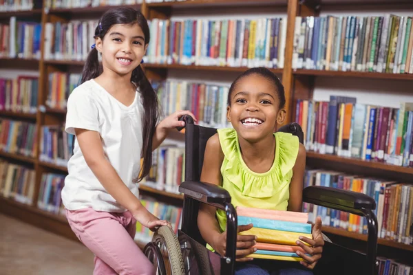 Улыбающийся ученик в инвалидной коляске держит книги в библиотеке — стоковое фото