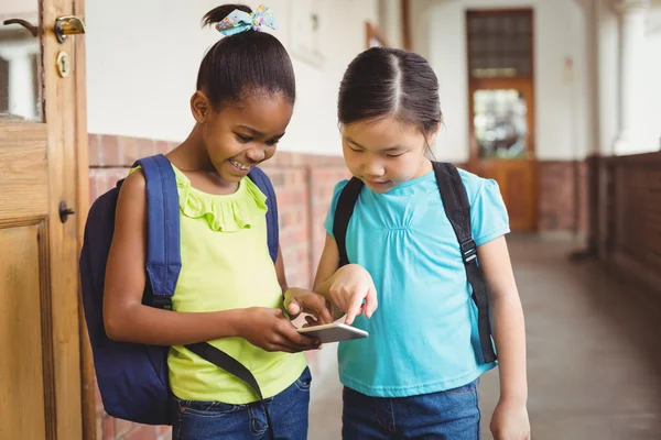 Niedliche Schüler schauen auf dem Flur aufs Smartphone — Stockfoto