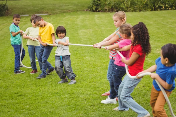 Cute pupils playing tug of war on the grass outside — Stock Photo, Image