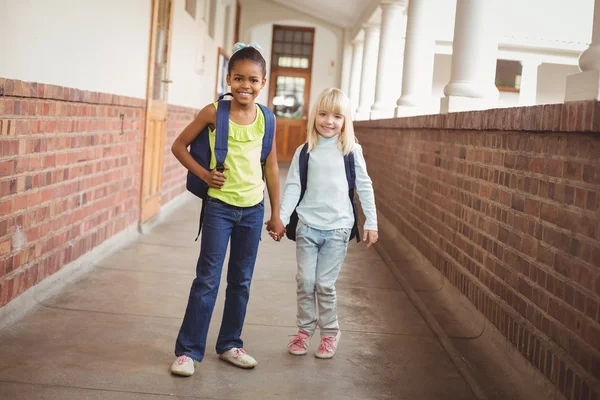 Smiling pupils holding hands at corridor — Stock Photo, Image