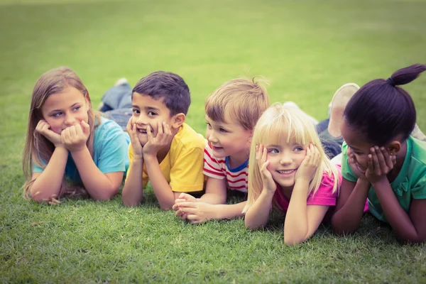 Smiling classmates lying in a row in grass — Stock Photo, Image