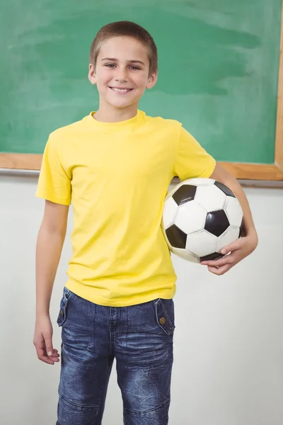 Usmívající se žák drží fotbal v učebně — Stock fotografie