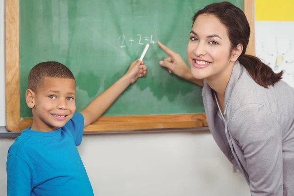 Pěkná učitelka pomáhá žáků na tabuli — Stock fotografie