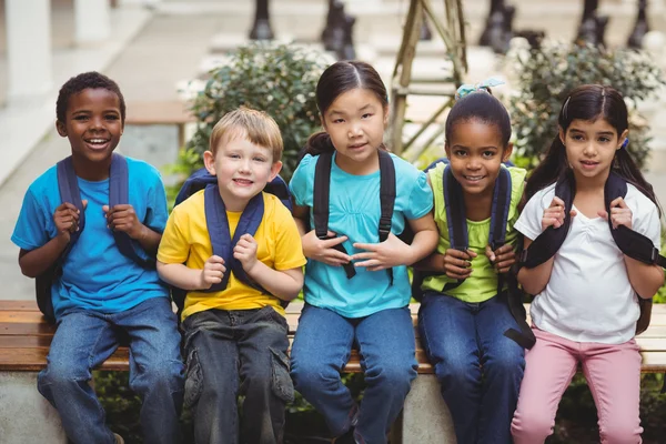 Happy pupils with schoolbags sitting on bench — Stock Photo, Image