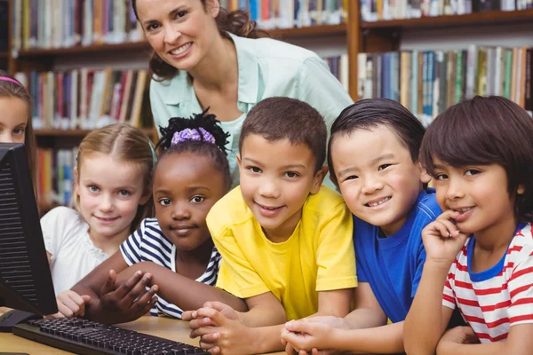 Pupils and teacher in library using computer — Stock Photo, Image