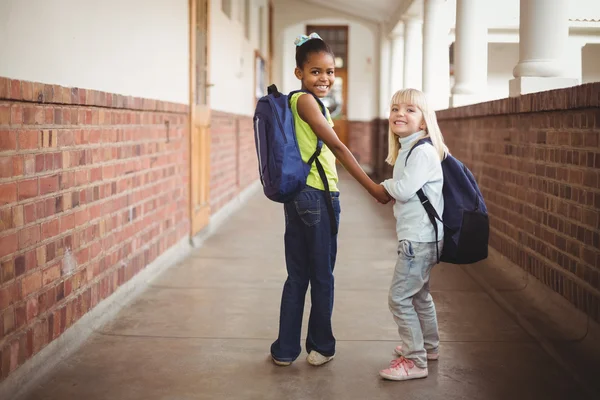 Smiling pupils holding hands at corridor — Stock Photo, Image