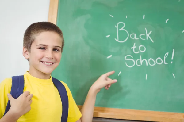 Smiling pupil pointing on back to school sign on chalkboard — Stock Photo, Image
