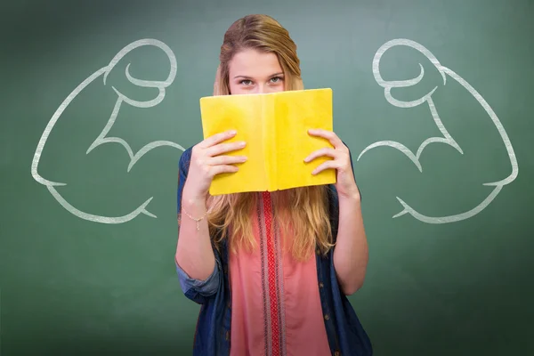 Student covering face with book in library — Stock Photo, Image