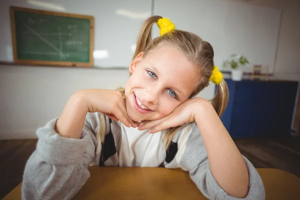 Leende elev sitter vid hennes skrivbord i ett klassrum — Stockfoto