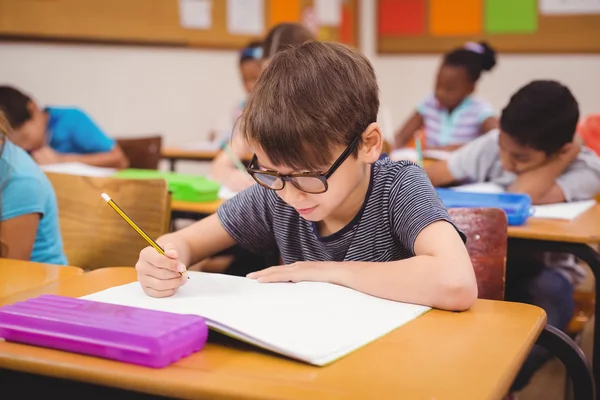 Liten pojke arbetar vid sitt skrivbord i klass — Stockfoto