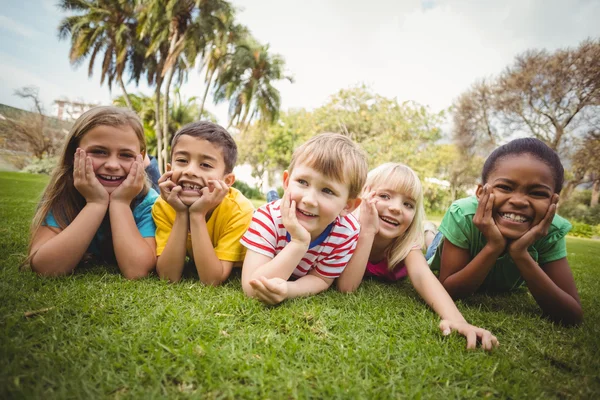 Lächelnde Klassenkameraden liegen in einer Reihe im Gras — Stockfoto