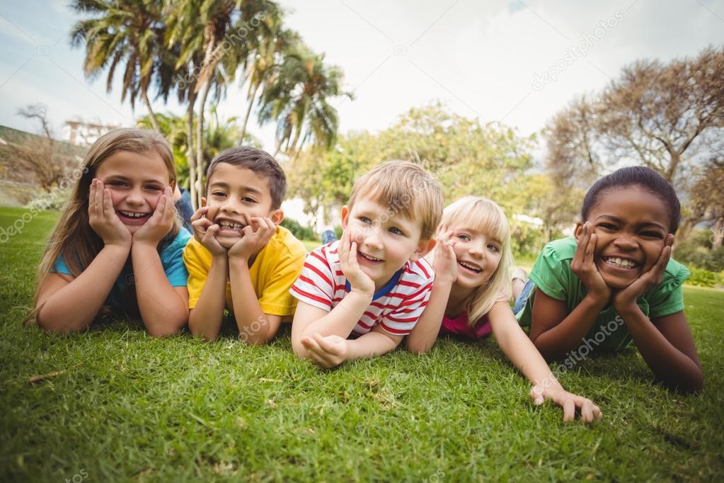 Smiling classmates lying in a row in grass — Stock Photo © Wavebreakmedia #84706354 Smiling classmates lying in a row in grass