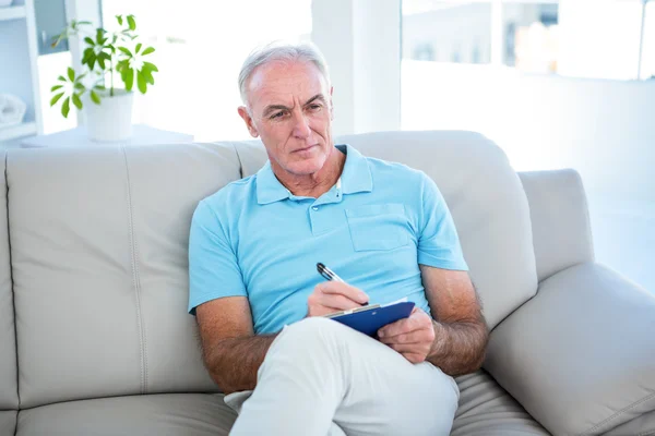 Thoughtful senior man writing on clipboard — Stock Photo, Image