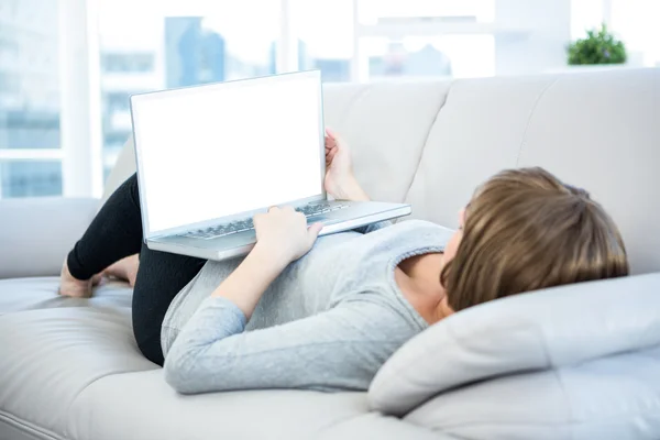 Woman using laptop while lying on sofa — Stock Photo, Image