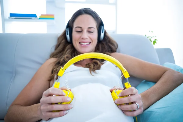 Mulher segurando fones de ouvido na barriga — Fotografia de Stock