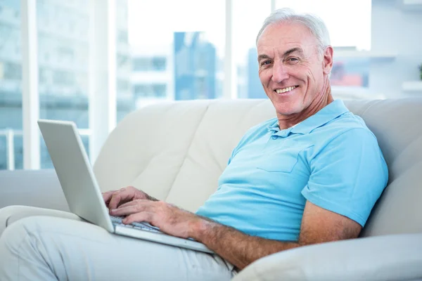Uomo anziano seduto sul divano con computer portatile — Foto Stock
