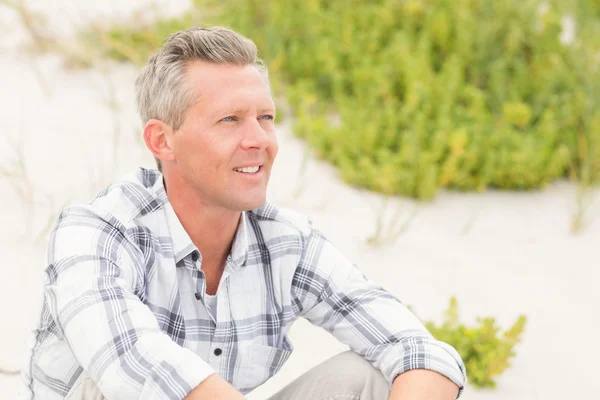 Homem sorridente sentado na areia — Fotografia de Stock