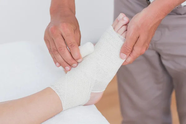 Doctor bandaging his patient ankle — Stock Photo, Image