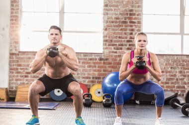 muscular serious couple with kettlebells clipart